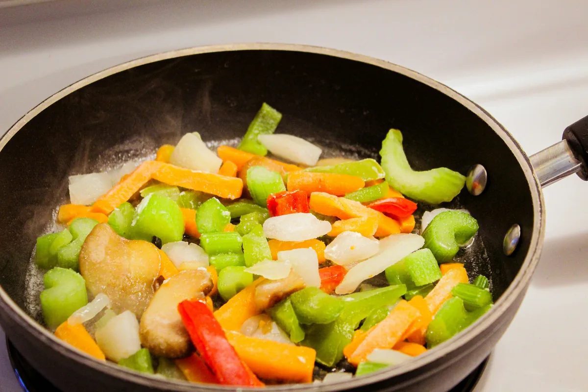 Chopped vegetables sautéing in a frying pan on the stove