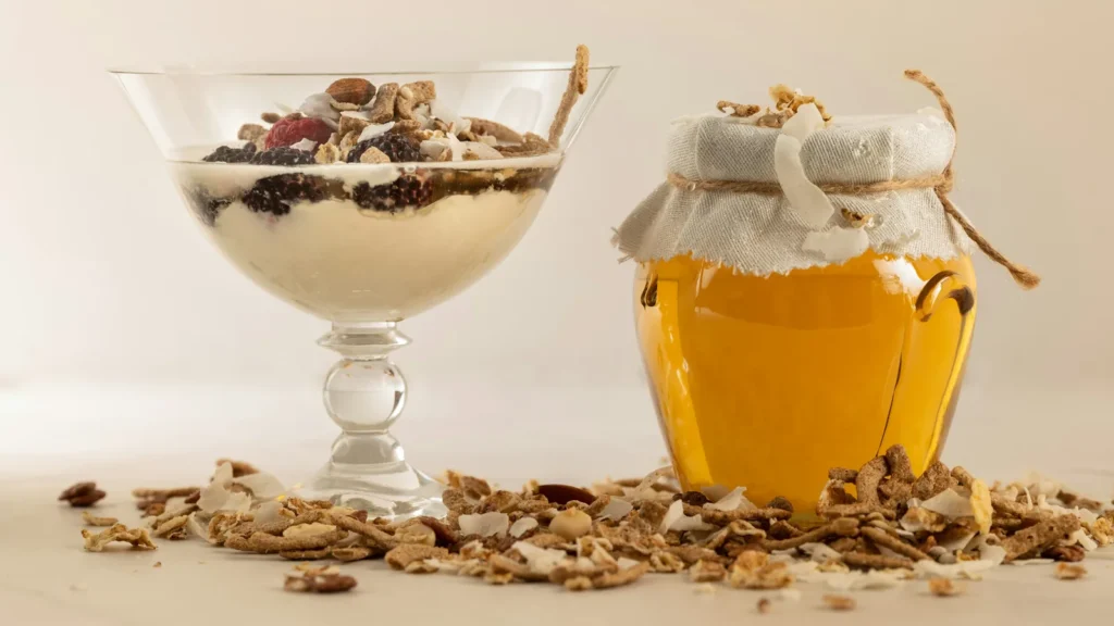 Glass of yogurt topped with nuts beside a jar of honey, a simple Greek yogurt with honey dessert