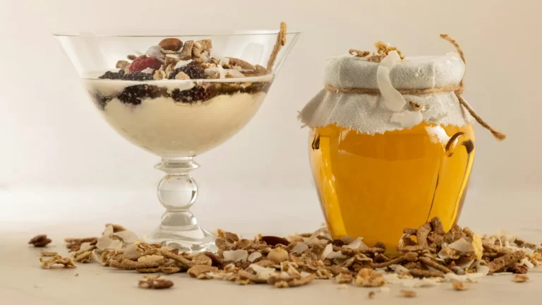 Glass of yogurt topped with nuts beside a jar of honey, a simple Greek yogurt with honey dessert