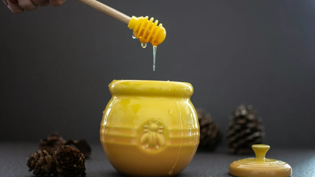 Yellow honey pot with a dipper of honey, asking is creamed honey dairy free