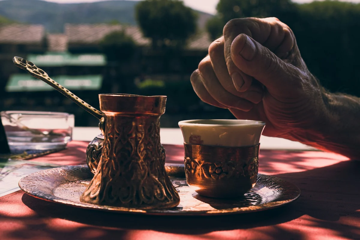 Greek coffee served from a copper briki into a small cup at an outdoor table