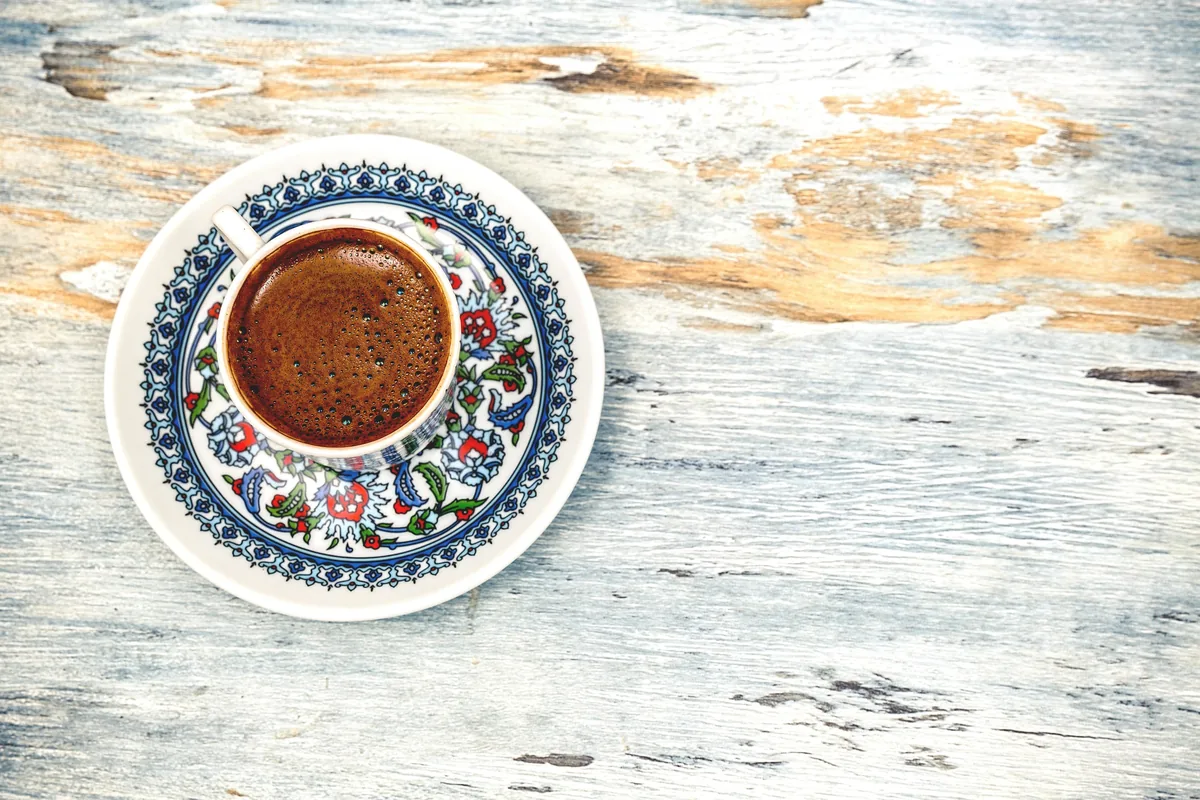 Top view of a cup of Greek coffee with foam on a patterned saucer