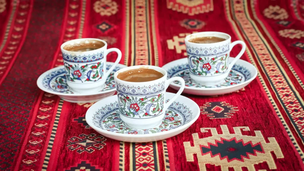 Cups of foamy coffee on a red patterned rug, the shared tradition behind Greek coffee vs Turkish coffee