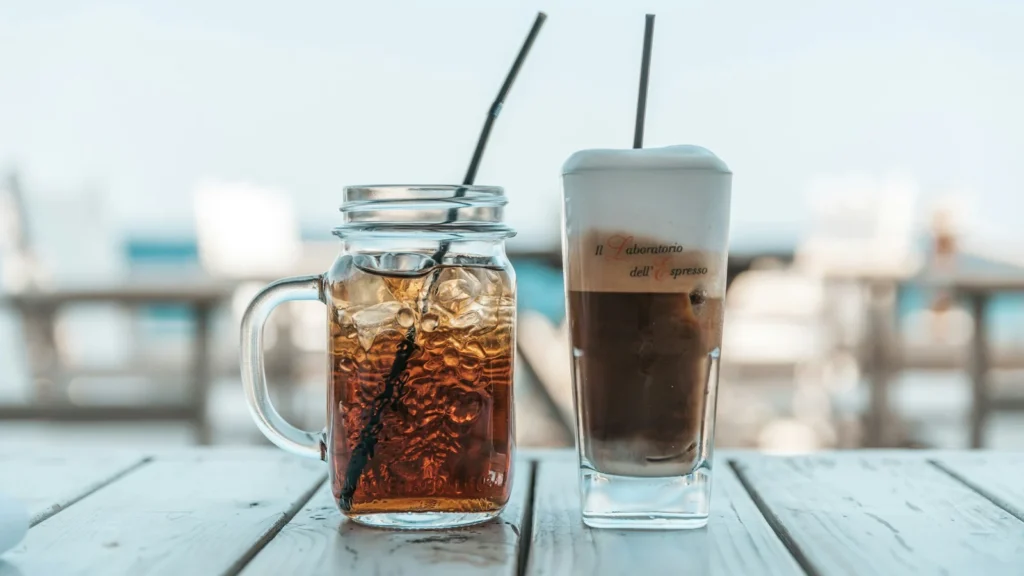 Greek frappe iced coffee with foam next to an iced drink on a seaside table