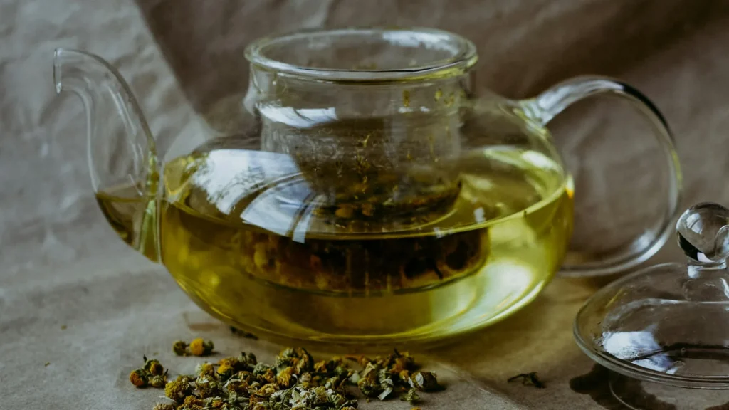Glass teapot of golden herbal tea with dried leaves, for reading about Greek mountain tea benefits
