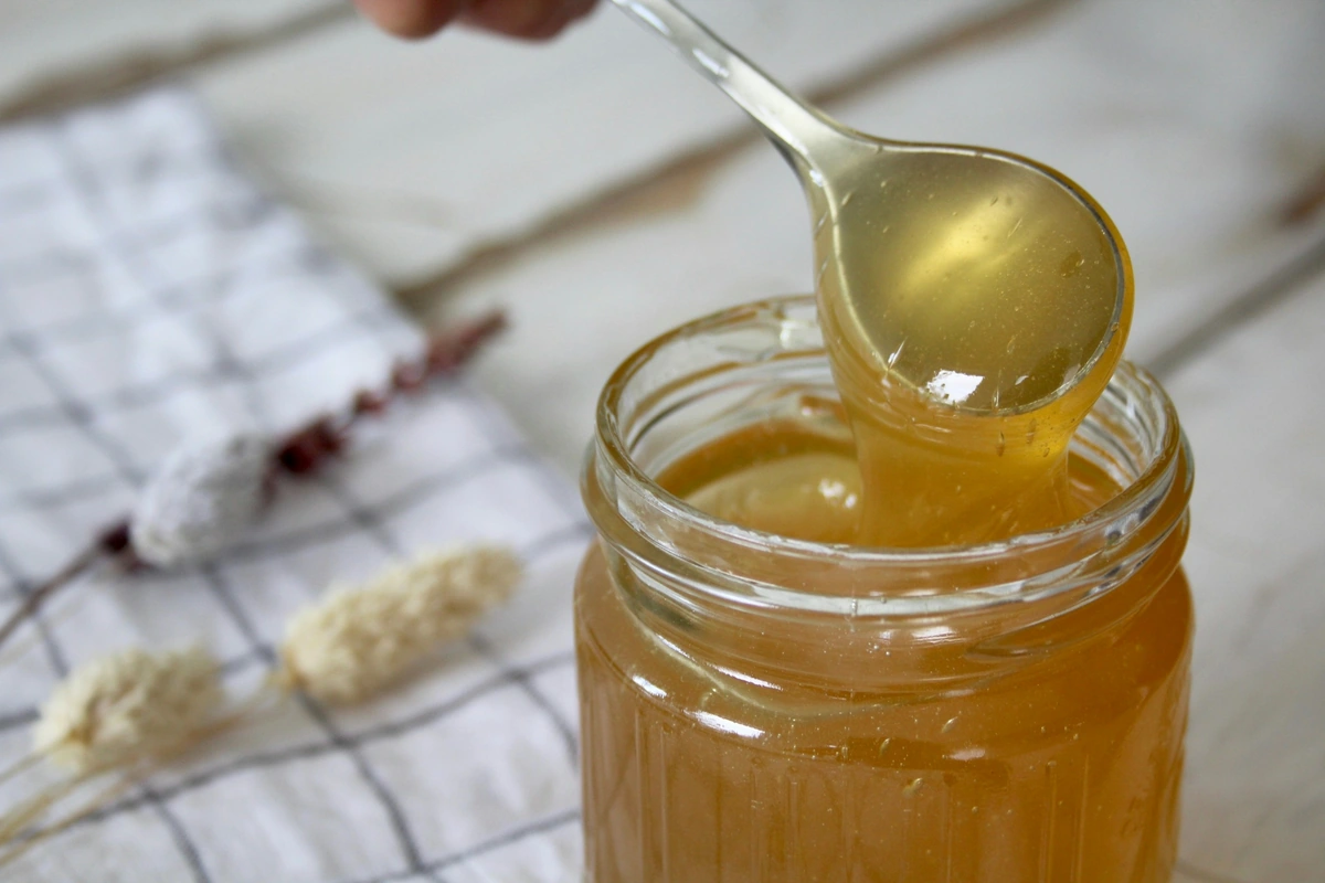 Spoon lifting honey from a glass jar at breakfast