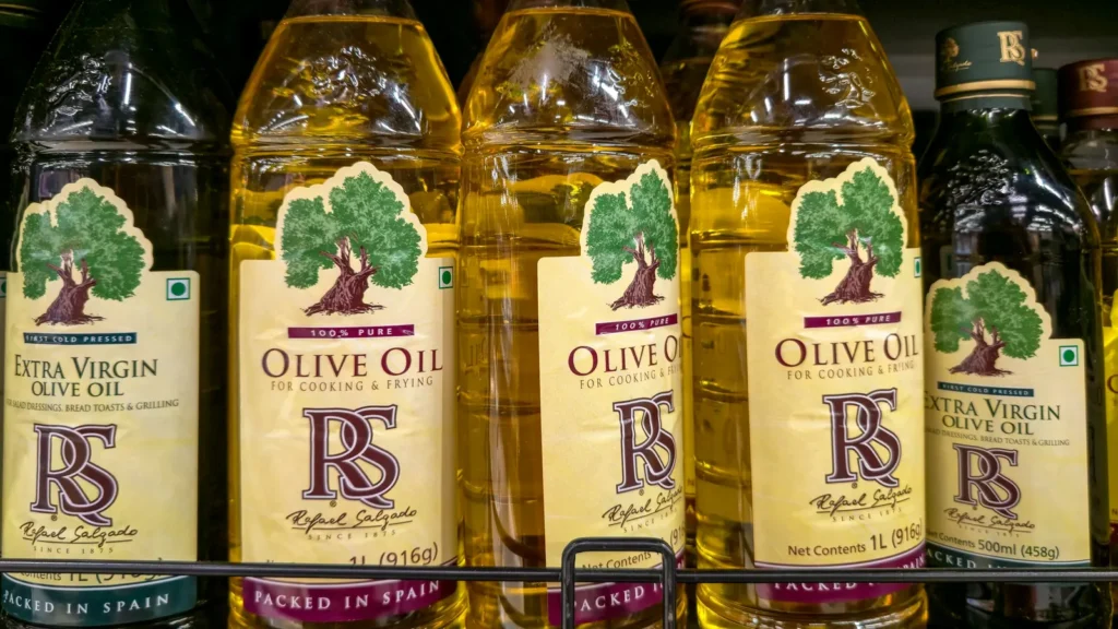 Rows of retail olive oil containers on a shop shelf, for comparing olive oil tin vs glass bottle