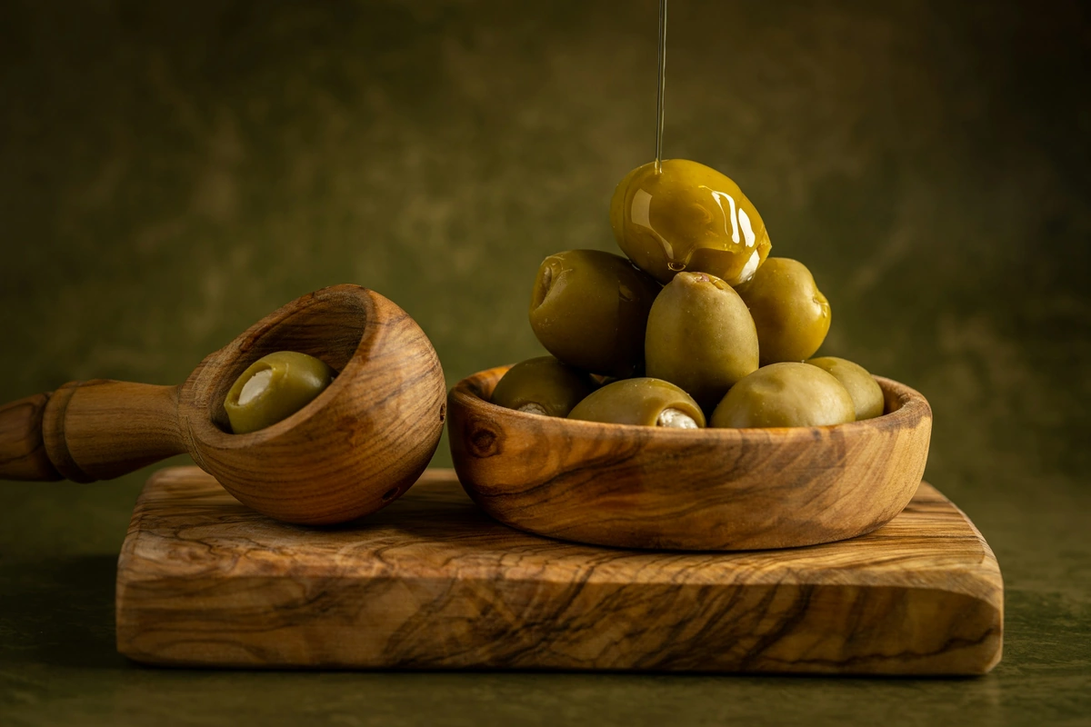 Green olives in a wooden bowl and spoon on a board