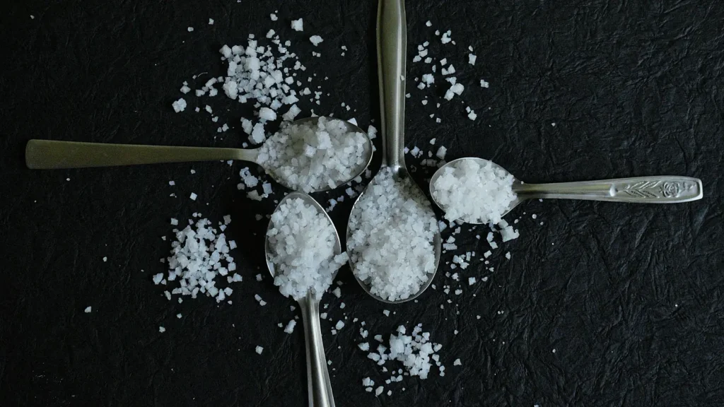 Spoons of sea salt flakes vs ground sea salt on a dark surface